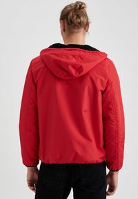 Červená bunda s kapucí, měkkou černou fleecovou podšívkou, elastickými manžetami a zipem. Hladký vnější materiál, zkrácený střih a minimalistická konstrukce.