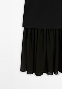 Schwarzes Kleid mit einem taillierten Oberteil und einem plissierten, fließenden Rock. Der Stoff hat eine glatte Textur und eine halbtransparente Überlage am Saum.