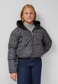 Grijze pufferjas met een zwart luipaardprintpatroon, voorzien van een rits en capuchon. Gedragen over een grijze sweater en blauwe jeans.