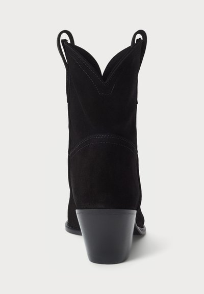 Bottine de cowboy en suédine noire avec un bout pointu et un haut festonné. Équipée de petites anses et d'un talon empilé pour plus de stabilité.