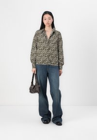 Grønn skjorte med blomstermønster og knapper, lange ermer, brukt sammen med blå vide jeans og en liten brun skulderveske.