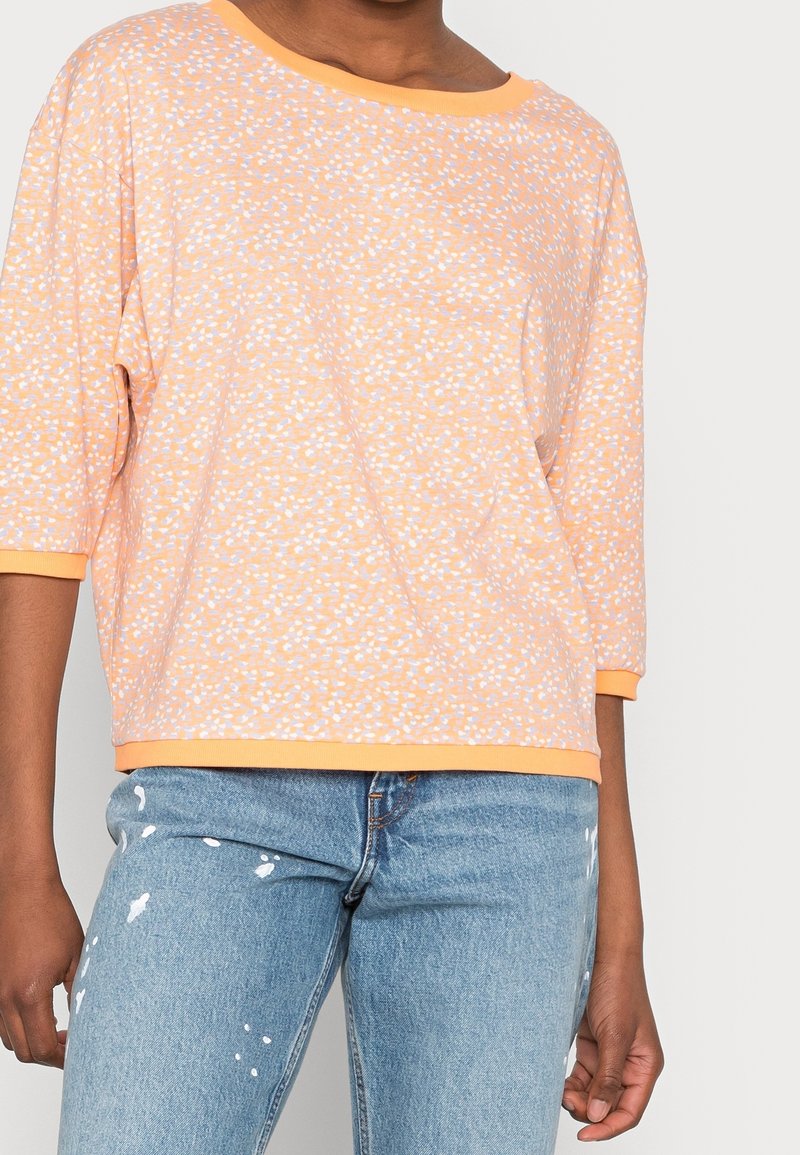 Orange top with white and light blue speckled pattern, wide neckline, three-quarter sleeves, soft fabric, and a relaxed fit.