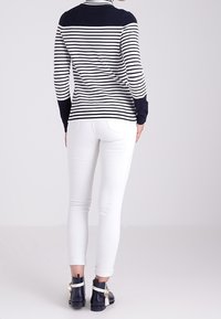 Sweter w paski w kolorze navy i białym, z wysokim kołnierzem i długimi rękawami, w zestawieniu z białymi slim-fit spodniami i czarnymi botkami za kostkę.