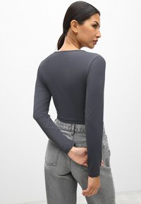Grijze lange mouwen top gemaakt van gladde, rekbare stof, gecombineerd met hoogwezige grijze denim jeans met achterzakken en een gestructureerde afwerking.