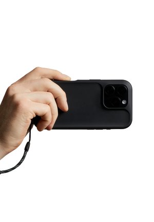 Hand holding a black smartphone with triple camera lenses and a wrist strap against a white background.