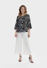 Top nero con motivo floreale bianco, vestibilità ampia, maniche a campana, abbinato a pantaloni bianchi a gamba larga e sandali neri con tacco alto.