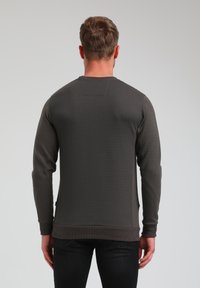 Felpa grigio scuro in tessuto con maniche lunghe e polsini a costine, caratterizzata da un design semplice e un discreto dettaglio della tasca sul retro.