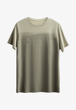 Olijfgroene t-shirt met korte mouwen, voorzien van een subtiele gradientontwerp en een bedrukt illustratie van een figuur die langs een hek loopt.