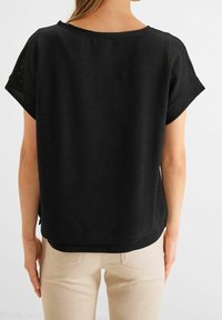 Svart kortärmad topp i strukturerad våffelstickad tyg. Har en bred halsringning och en avslappnad passform, med en rundad nederkant.