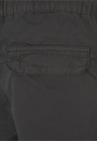 Crne kratke hlače od lagane tkanine, s stražnjim džepom s preklopom. Površina ima glatku teksturu i minimalne detalje šivanja.