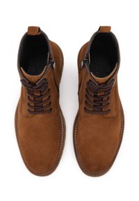 Stivaletti in suede marrone con punta tonda, lacci marroni scuri, cerniera laterale e dettagli cuciti attorno alla suola. Texture morbida in tutto il prodotto.