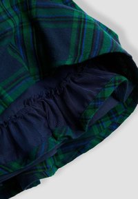 Grünes und navy blaues Karostoff mit elastischem, gerafftem navy Mesh-Futter im Inneren eines Kleidungsstücks.