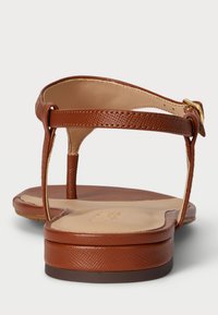 Hnedé kožené sandále s textúrovaným povrchom, dizajnom t-pásika, nastaviteľným prackom a plochou podrážkou. Majú odolný a hladký interiér.