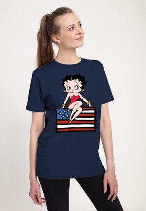 Camiseta azul marino con un personaje de dibujos animados, vestido con un traje rojo, sentado sobre un diseño de bandera a rayas en rojo, blanco y azul.