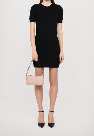 Eine Frau trägt ein eng anliegendes schwarzes kurzes Kleid und hält eine pinke Michael Kors Handtasche, kombiniert mit schwarzen spitzen Absatzschuhen mit Knöchelriemen.