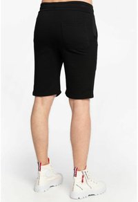 Schwarze Baumwollshorts mit schlanker Passform, ausgestattet mit einer Gesäßtasche und einer glatten Textur. Getragen mit weißen High-Top-Sneakern.