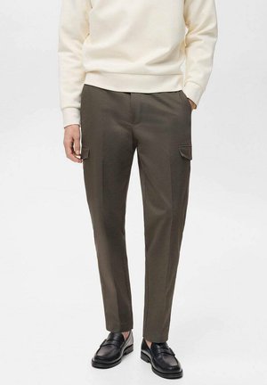 Pantaloni cargo verde oliva con due tasche laterali, realizzati in un tessuto morbido e leggero; abbinati a un maglione beige chiaro e mocassini neri.