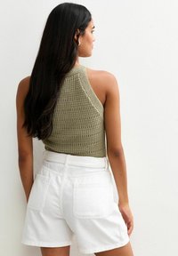 Top en maille olive à motif texturé, associé à un short en denim blanc taille haute avec des poches arrière.