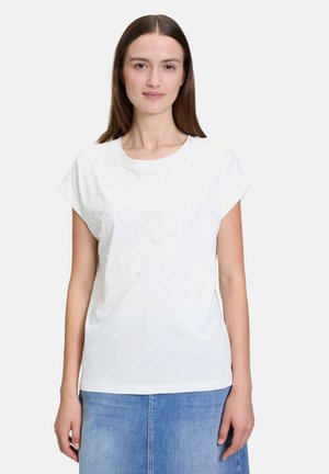 T-shirt blanc à manches courtes présentant des embellissements texturés sur le devant. Tissu doux, col rond et coupe décontractée. Associé à une jupe en denim.
