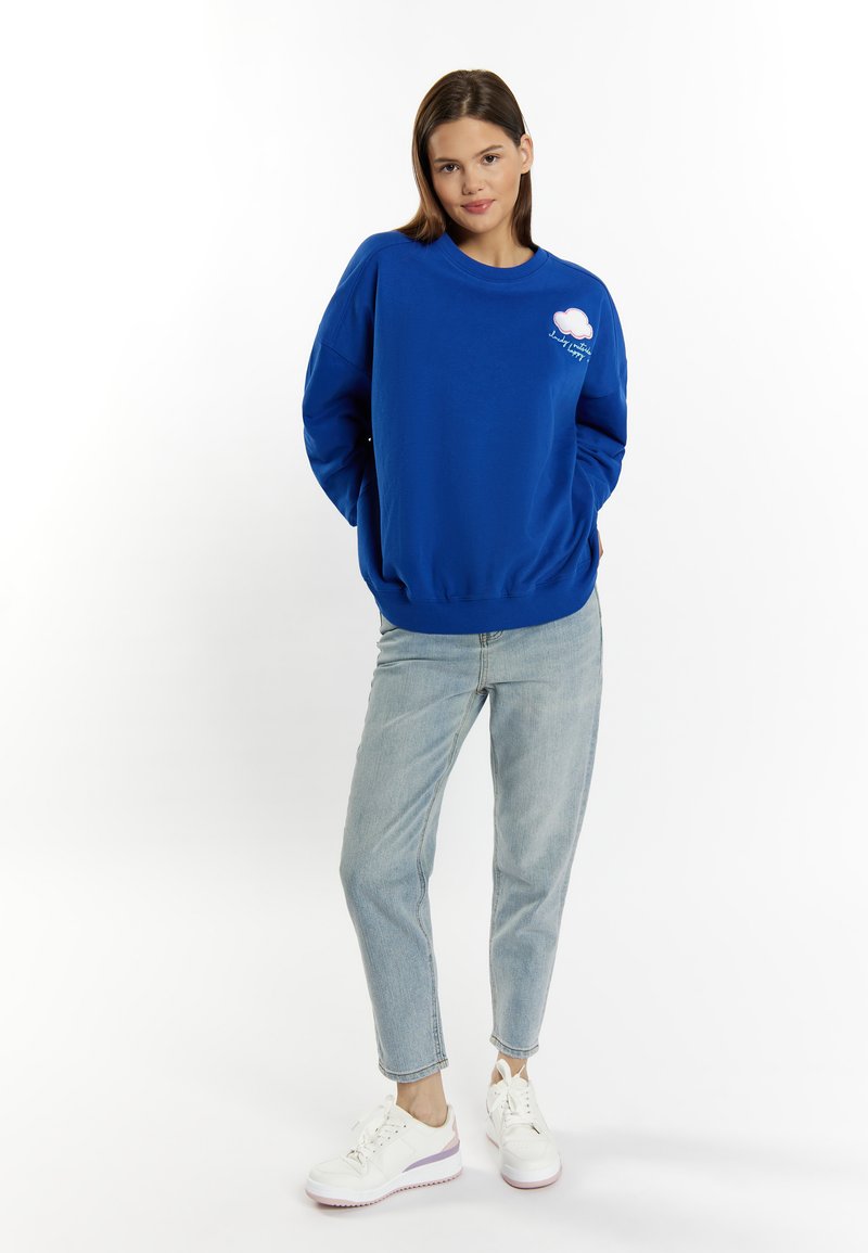 Felpa blu in cotone morbido con collo rotondo, caratterizzata da una grafica di una nuvola bianca e dettagli ricamati, abbinata a jeans azzurri chiari.