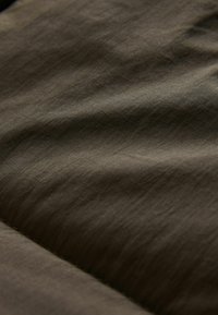Tissu texturé dans une teinte vert olive foncé, présentant des plis subtils et une surface légèrement lumineuse, mettant en valeur une finition douce et mate.