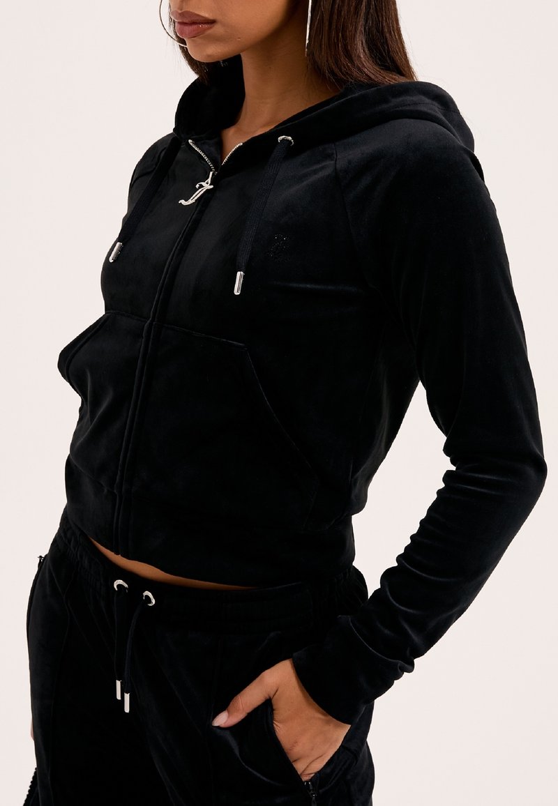 Sort velour zip-up hoodie med en frontlomme, tætsiddende design og justerbare snore. Har sølv hardware og en diskret logo-detail.