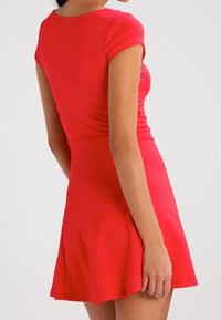 Robe rouge à manches courtes avec un corsage ajusté et une jupe évasée. Tissu texturé avec une finition lisse et des détails de couture subtils à la taille.