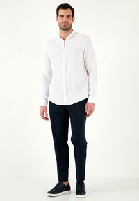 Camisa blanca de botones con cuello mao, tejido texturizado, combinada con pantalones oscuros de color azul marino y zapatillas negras.