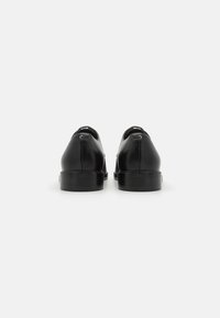 Black leather shoes with a smooth finish, round toe, and a low heel. Rear view shows stitching detail and small hardware accents.