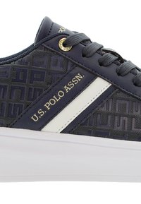 Marinblå sneakers med präglat mönster, vita detaljer, guldlogotyp. Har runda snörningar och texturerad gummisula.
