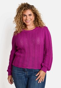 Pull en tricot violet vibrant avec un motif en vagues, présentant des poignets côtelés et un col rond. La texture est aérée et légère.