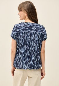 Blusa blu navy con un motivo astratto azzurro, maniche corte e dettagli plissettati sul retro, realizzata in tessuto morbido e leggero.