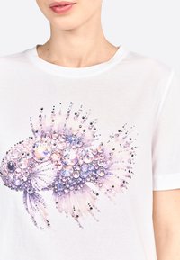 Tricou alb cu un grafic detaliat al unui pește decorat cu mărgele strălucitoare în culori purpurii și transparente, creând un efect texturat și strălucitor.