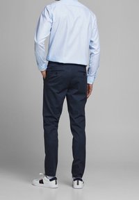 Jasnoniebieska koszula z długim rękawem i mankietami na guziki, zestawiona z ciemnogranatowymi spodniami. Białe sneakersy z granatowymi i czerwonymi akcentami. Gładkie faktury.