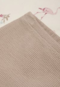 Beige ribbad tyg med fin horisontell textur; synlig söm längs kanten; bakgrunden har ljusa blommönster och flamingonöter.