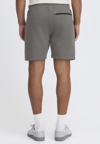 Shorts gris avec une texture douce, comportant une poche arrière zippée et une taille élastique. Assortis avec des chaussures grises et des chaussettes blanches.