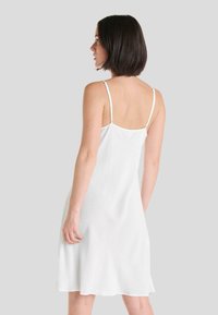 Vestido blanco sin mangas con un corte relajado, que presenta tirantes finos y un tejido ligeramente texturizado. La línea del dobladillo cae por encima de la rodilla.