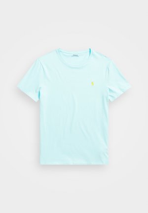 Jasnoniebieski t-shirt z krótkim rękawem i okrągłym dekoltem, z małym żółtym haftowanym logo na lewej piersi, leżący płasko na białym tle.