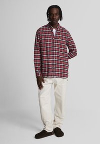Camicia a quadri rossa e blu, con maniche lunghe, t-shirt bianca sotto, abbinata a pantaloni color crema e zoccoli marrone scuro.