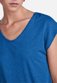 Camiseta de cuello en V azul con mangas cortas, que presenta un patrón texturizado de líneas horizontales y un acabado de tela suave.