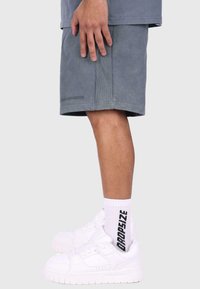 Grå kordshorts med et side-seam logo og hvide sneakers kombineret med hvide ribbede sokker med sort tekst.