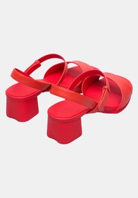 Punaiset korkokengät matalla, sileällä pinnalla. Varustettu kahdella ohuella nauhalla edessä ja säädettävällä nilkkahihnalla. Neliömäiset platform-korkot.