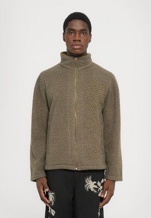Olivgrüne, durchgängige Jacke mit hohem Kragen, strukturiertem Stoff und goldenen Nietenverzierungen, die ein dekoratives Muster auf der Vorderseite bilden.