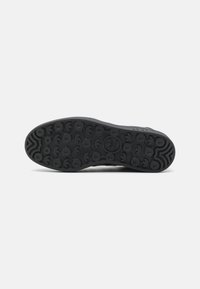 Černá gumová podrážka boty s kruhovým vzorkem a centrálně umístěným logem Adidas, zobrazená na jednoduchém bílém pozadí.