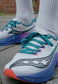 Sneakerid valge võrgust pealmise osaga, millel on teal'i tooni aktsendid, lillakates gradatsioonides vaheosa ja ainulaadne graafiline muster. Küljest ühendatud valged sokid.