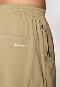 Beige shorts made of lightweight fabric, featuring an elastic waistband, side zipper pocket, and 'snow peak' logo in white.