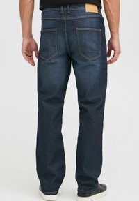 Jeans de mezclilla azul oscuro con un corte recto, que presentan dos bolsillos traseros, costuras sutiles y una etiqueta de cuero marrón en la cinturilla.