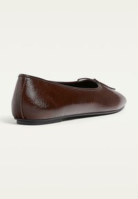 Ballerine en cuir marron avec une texture lisse, bout rond et un petit nœud à l'avant. Semelle en caoutchouc noire basse.
