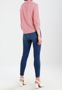 Rød og hvidstribet bluse med lange ærmer og knapmanchetter, parret med blå skinny jeans og hvide hælede sandaler.