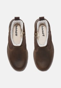 Barna bőr, slip-on stílusú cipők, bolyhos béléssel, oldalsó cipzárokkal és lekerekített orral. Párnázott talpbéléssel és varrott részletekkel rendelkezik.